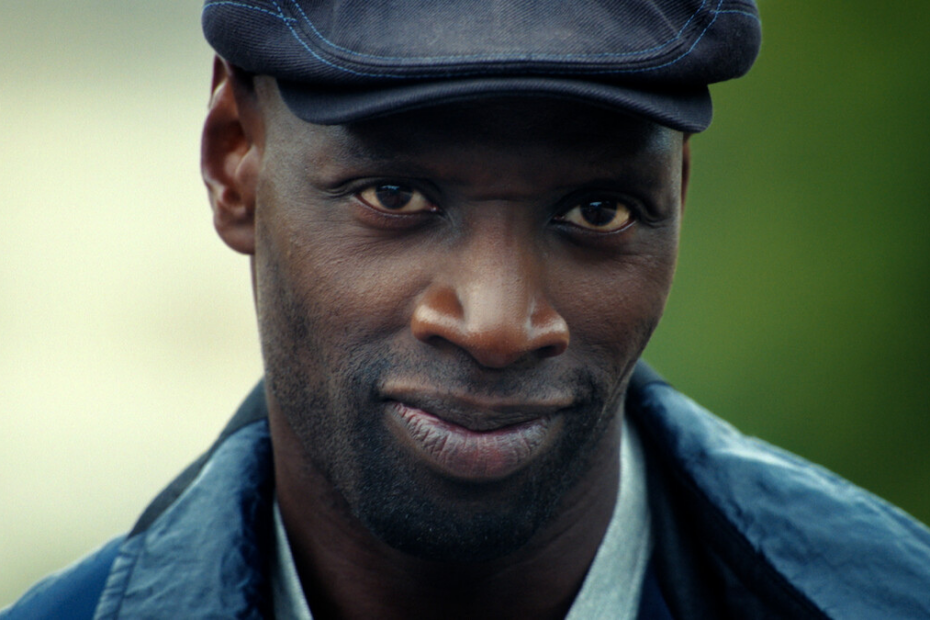 Omar Sy în rolul lui Assane Diop, cu șapcă închisă și jachetă albastră, în Lupin, partea 4.